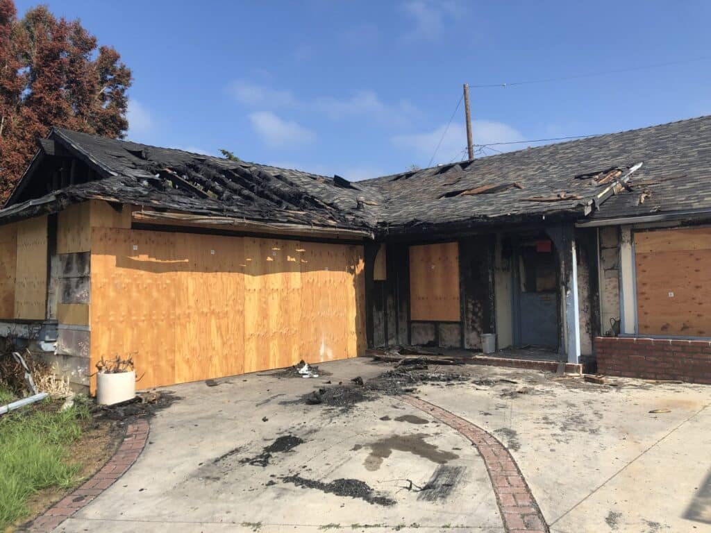 Plywood covering openings at a house with visible roof and fire damage